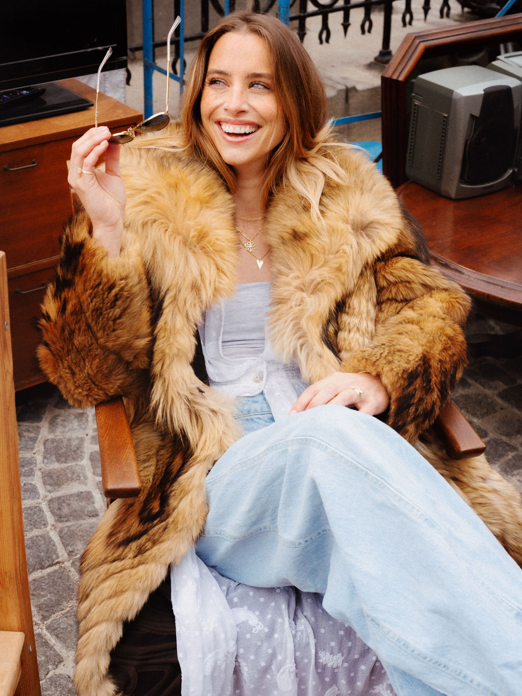 Woman wearing a fur coat sitting on a bench outdoors.