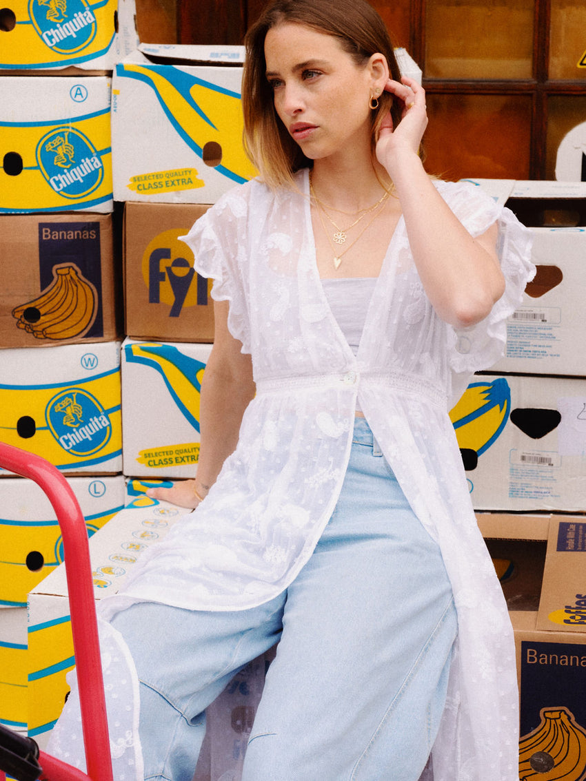 Woman in a white shirt and light blue jeans sitting among stacked banana boxes.