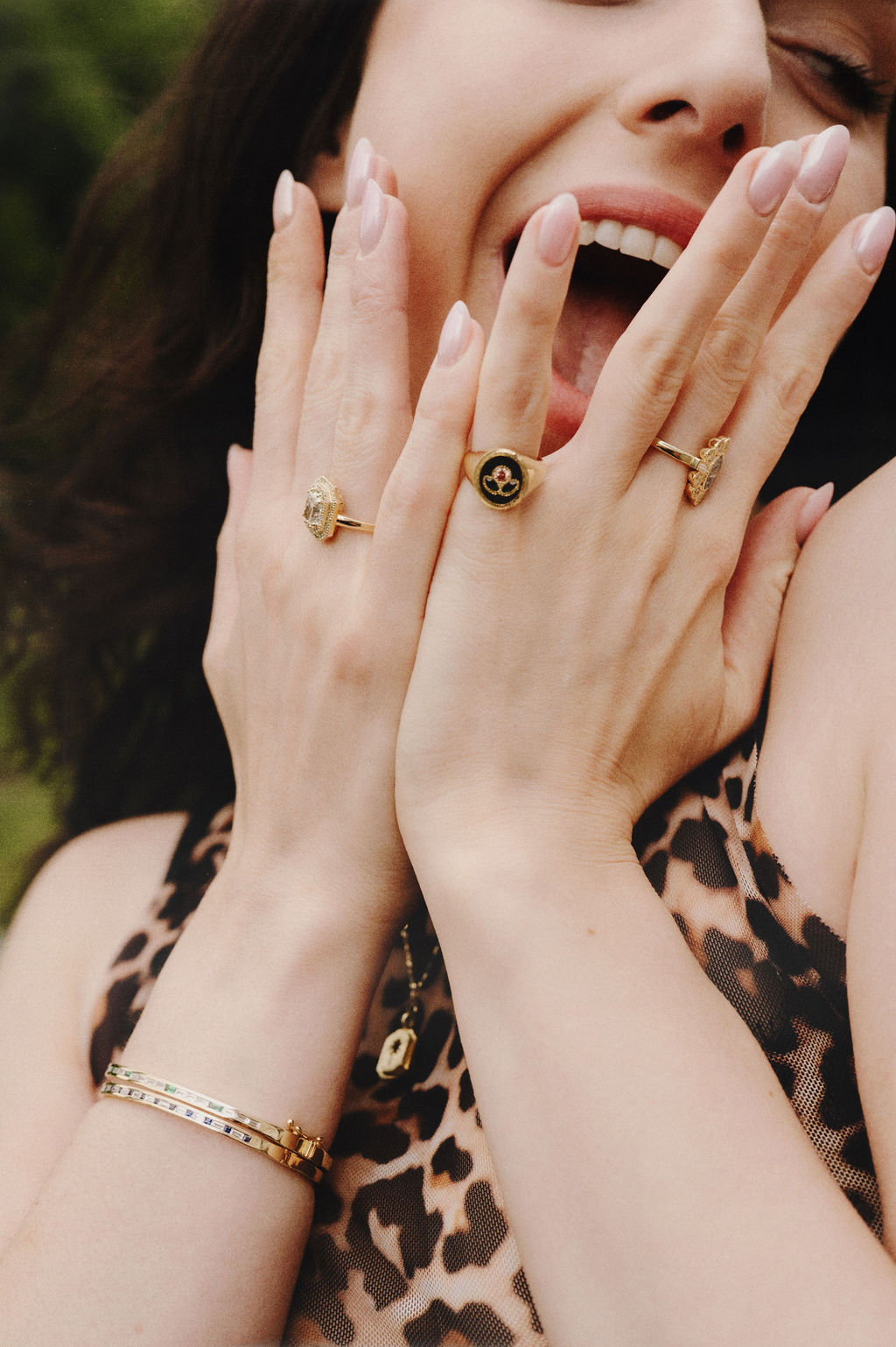 Woman with gold rings and bracelets covering her mouth, wearing a leopard print top.
