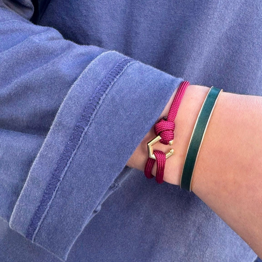 Close-up of a wrist wearing a red bracelet with a gold clasp and a green band, against a blue denim background.