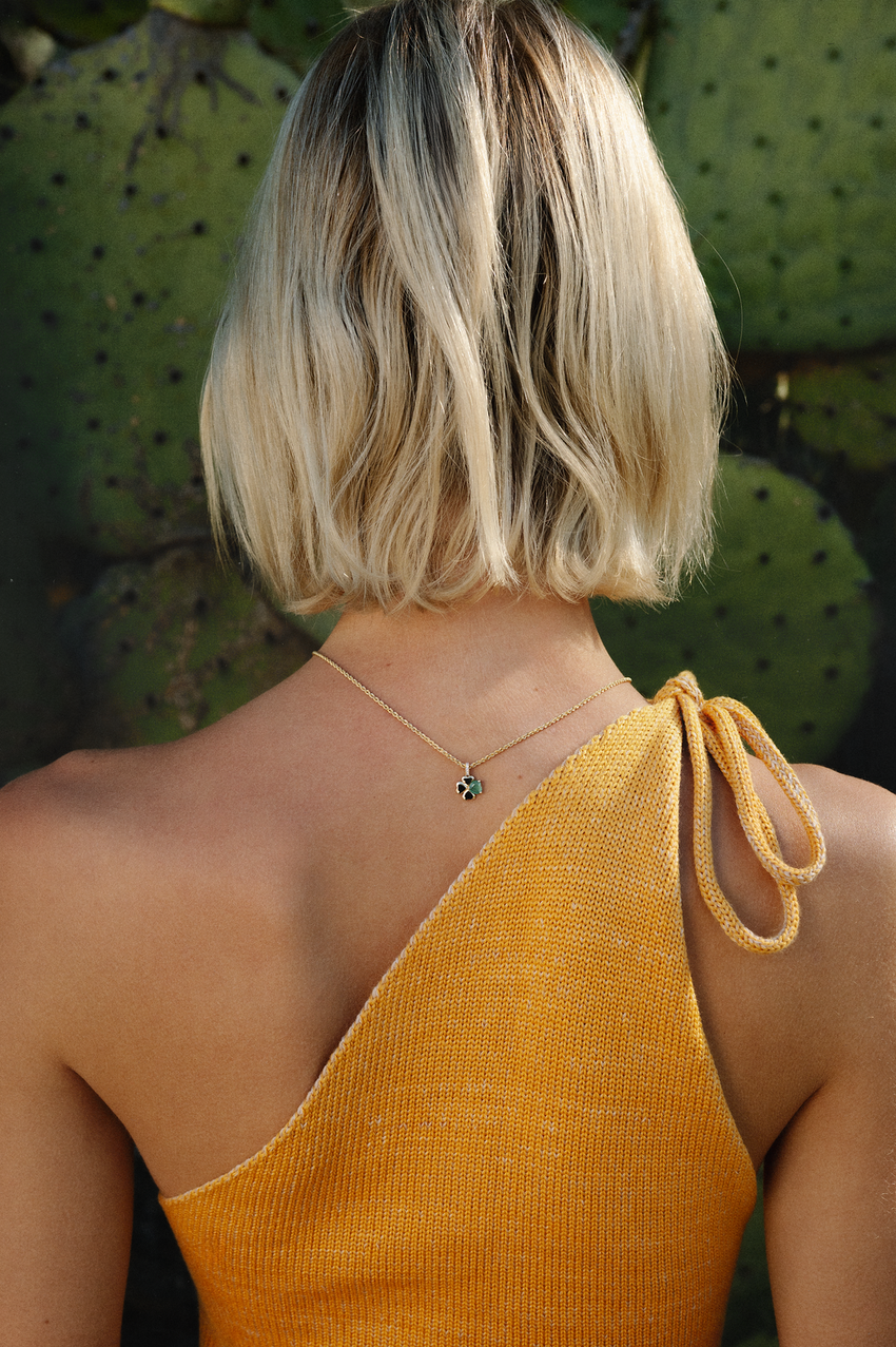 Person wearing a mustard yellow one-shoulder top with a cactus plant in the background