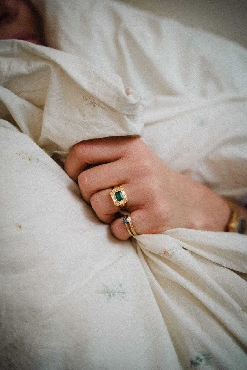 Close-up of a hand wearing gold rings with green gemstones on a white fabric background